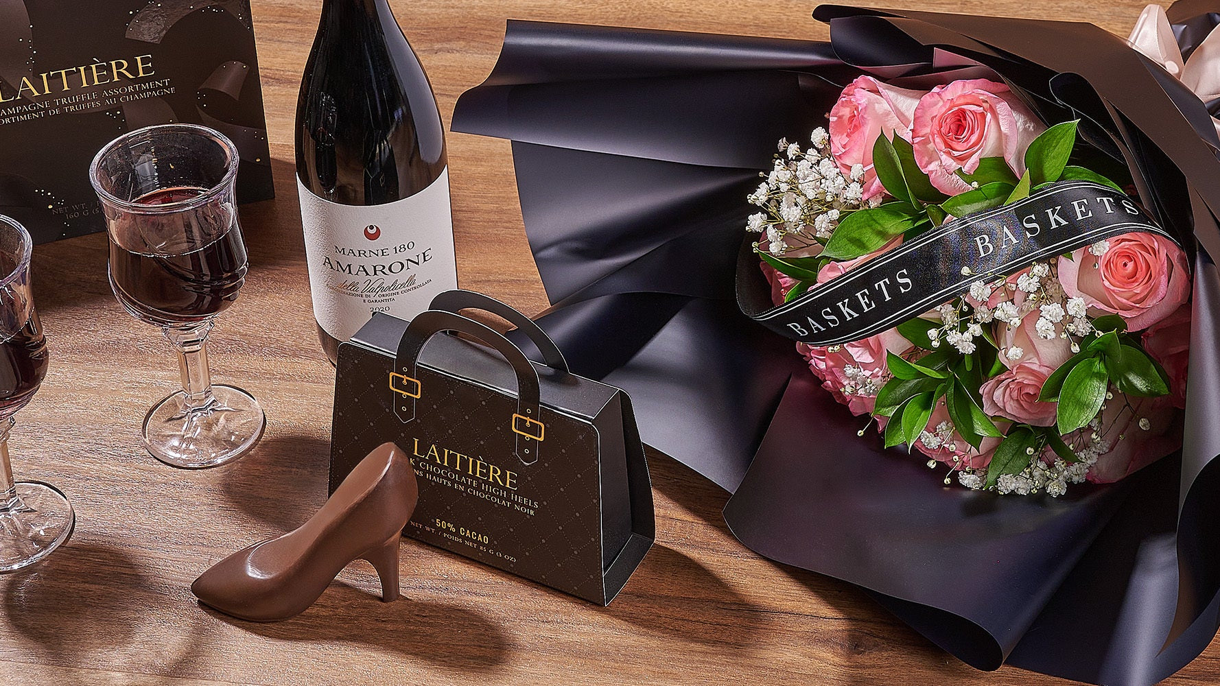 Bouquet of pink roses, wine glasses, and a bottle on a wooden surface.